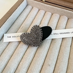 Close-up of heart-shaped hair clip with grey rhinestones on a beige velvet background
