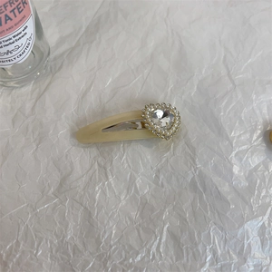 Detail of a creamy yellow heart-shaped rhinestone BB hair clip on textured paper
