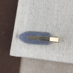 Détail d'une pince à cheveux dorée avec finition en tissu pailleté gris sur fond neutre