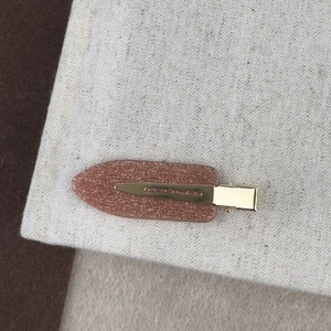 Détail de la pince à cheveux pailletée bronze posée sur un tissu en lin texturé