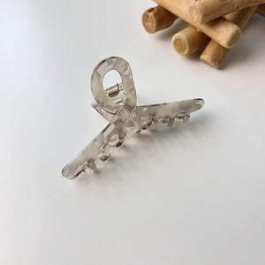 Détail d'une pince à cheveux en acétate marbré gris avec ressort doré sur un bureau