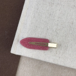 Gros plan d'une pince à cheveux rose pailletée avec base dorée sur un tissu texturé fin
