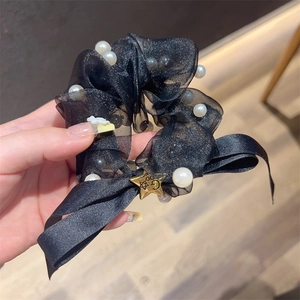 Nahaufnahme von schwarzem Organza-Haargummi mit Perlen und goldenem Stern-Anhänger