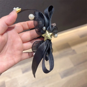 Nahaufnahme eines schwarzen Schleifen-Haargummis mit Perlen und goldenem Good Luck-Stern-Anhänger