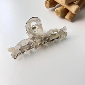 Pince à cheveux minimaliste en acétate à motif marbre avec ressort doré sur fond blanc