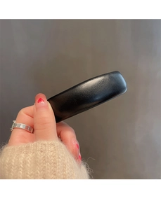 Detail view of a black rectangular leather-textured hair clip held against a gray wall