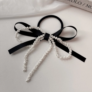 Elegante pinza per capelli con fiocco nero e perline bianche su sfondo di seta fine