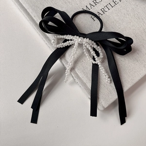 Detail of elegant black satin bow hair tie with delicate white pearl embellishments