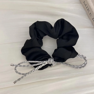 Détail du chouchou en satin noir avec nœud tressé argenté et texture fine et lisse