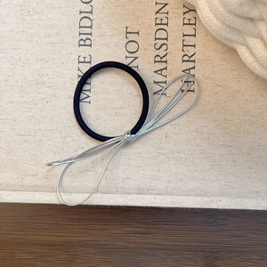 Détail d'un élastique à cheveux noir avec un nœud en métal argenté tissé sur bois