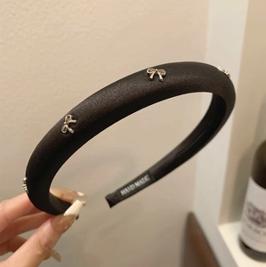 Padded black satin headband with decorative silver metal bows and handmade label detail