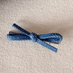 Detail view of denim bow hair clip showing blue fabric texture and metal spring clip