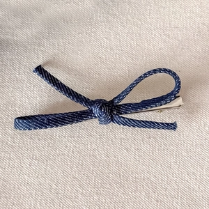 Close-up of deep blue denim bow hair clip with silver metal duckbill clip on linen