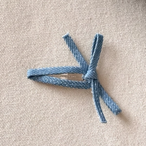 Detail of light blue denim bow hair clip with silver metal base on beige fabric
