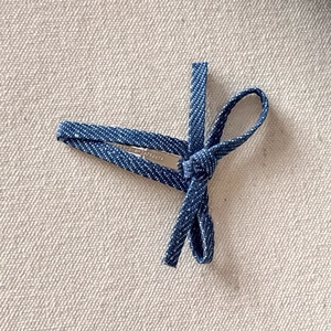 Detail view of deep blue denim fabric bow hair clip with silver metal alligator base