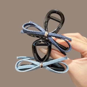 Detail showing two denim bow hair claws with metallic accents on polished black grip