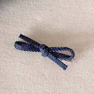 Detailed close-up of dark blue denim bow hair clip with silver metal clip base
