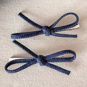 Detailed close-up of dark blue denim bow hair clips with silver metal alligator base