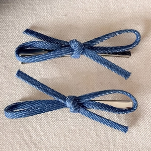 Detail view of two blue denim bow hair clips with silver metal duckbill base clips
