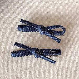 Close-up of deep blue denim fabric bow hair clips with twill texture and silver metal base