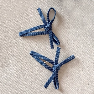 Detail of two blue denim bow hair clips showing textured fabric and metal duckbill grip