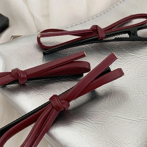 Three elegant wine red leather bow hair clips placed on a silver textured fabric