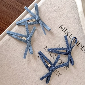 Bow-knot denim hair clips in light and dark blue on a textured fabric background