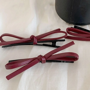 Three burgundy leather bow hair clips with textured finish on a white background