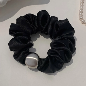 Detail of a black satin scrunchie with a silver metal bead on a gray background