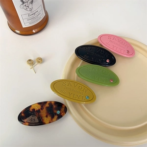 Macro detail of oval resin hair clips with relief lettering and small rhinestones