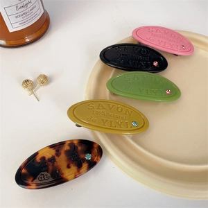 Detail of five oval hair clips in assorted colors with embossed text and sparkling rhinestones