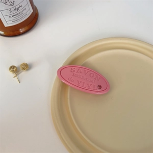 Close-up of pink oval hair clip with embossed text and sparkling pink rhinestone detail