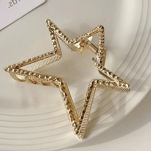Golden star-shaped alloy hair claw with hammered texture finish on a white plate