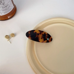 Close-up of tortoise shell hair clip with blue rhinestone on a beige ceramic plate