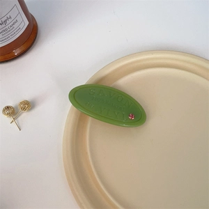 Close-up of green resin oval hair clip with SAVON text and pink rhinestone detail