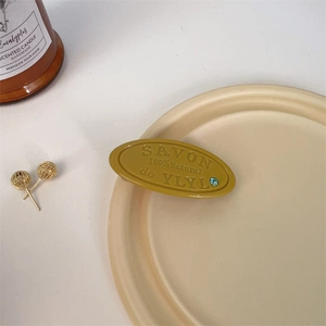 Detailed close-up of yellow oval cookie hair clip with blue rhinestone and embossed text
