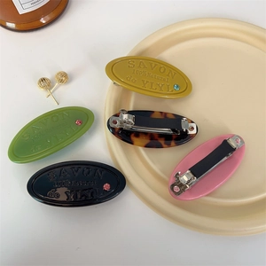 Detail of oval resin hair clips with relief letters and colorful rhinestones on a plate