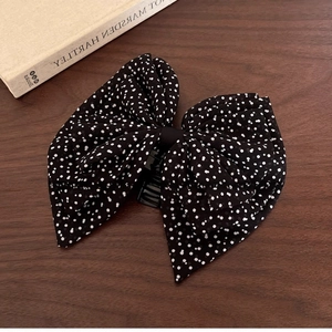 Polka dot bow hair claw clip in black and white fabric over a vintage wooden background