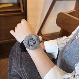 Détail d'un chouchou fleur de camélia gris avec perle blanche au poignet sous une lumière douce