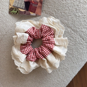 Detail of red plaid fabric and cream lace ruffles with floral embroidery on hair scrunchie