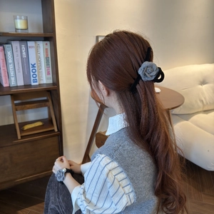 Détail d'une pince à cheveux camélia et d'un chouchou sur de longs cheveux bouclés