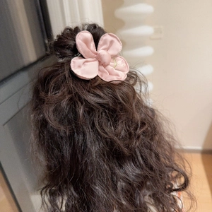 Pink fabric flower hair clip for kids and women worn on brown wavy hair in a cozy setting