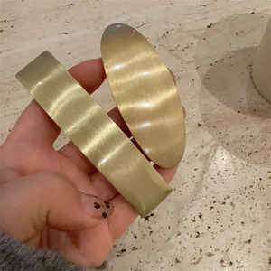 Minimalist matte gold metal hair clips with brushed texture held in hand over stone background