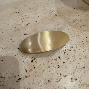Minimalist oval hair clip in brushed gold metal finish on elegant stone background