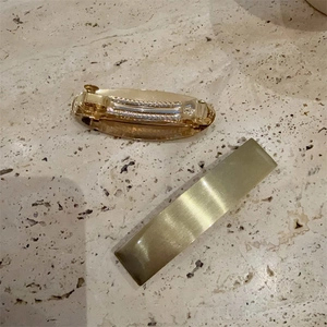 Golden rectangular and oval metal hair clip set on a textured stone background