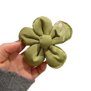 Hand holding green fabric flower hair clip with delicate pink floral embroidery detail