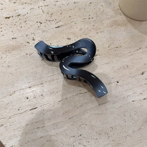 Elegant large black wavy hair claw clip for thick hair shown on a minimalist beige stone surface