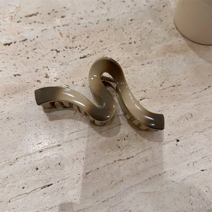 Elegant wavy gradient hair claw clip in brown and beige resin on a stone surface