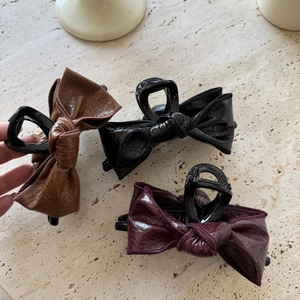 Close-up of three glossy leather bow hair claws in brown, black and burgundy colors