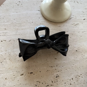 Glossy black leather bow hair claw clip with vintage texture on marble background